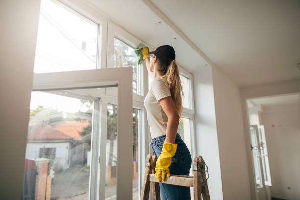 Woman in yellow gloves cleaning window with rag.